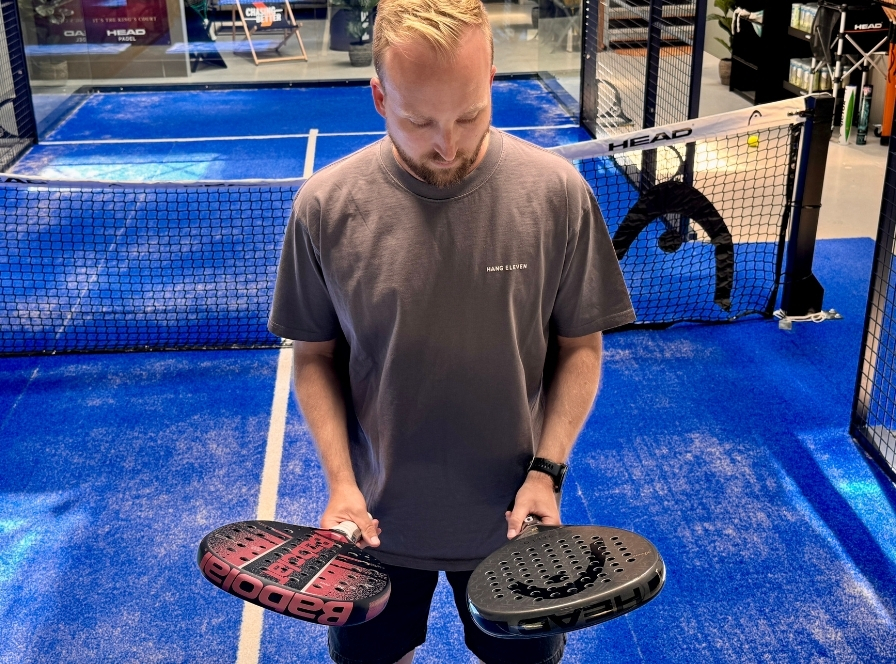 Mies pitelee vaaleanpunamustaa Babolat-padelmailaa ja mustaa HEAD-padelmailaa padelkentällä – aloittelijoiden mailavertailu
