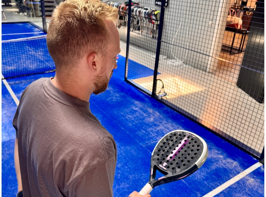 Mies testaa kokeneille pelaajille suunnattua padel-mailaa sisähallissa