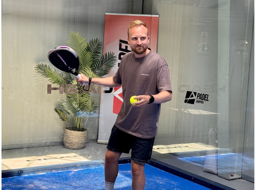 Padel-pelaaja pitelee mailaa ja palloa valmiina testaamaan kokeneiden pelaajien varusteita
